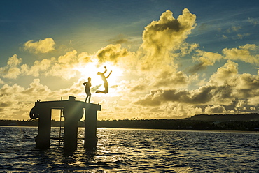 Backlit local boys jumping into the water of the lagoon of Wallis from a platform, Wallis and Futuna, Pacific