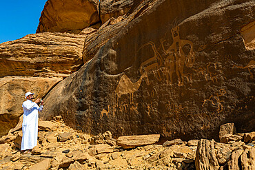 Man pointing at rock carvings, Bir Hima Rock Petroglyphs and Inscriptions, UNESCO World Heritage Site, Najran, Kingdom of Saudi Arabia, Middle East