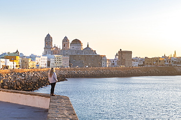 Woman enjoying the view of Santa Cruz Cathedral and ocean seen from the promenade along quayside, Cadiz, Andalusia, Spain, Europe