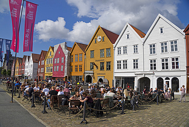 Tourists sit in the sun in outdoor bars and cafes in the old wharf and traditional wooden buildings in the Bryggen quarter of Bergen, UNESCO World Heritage Site, Norway, Scandinavia, Europe