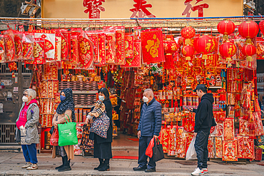 A shot of People wait at a bus stop underneath a Lantern and Lei see shop in Sheung Wan at Chinese New Year