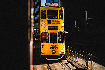 An artistic photograph of a Yellow Hong Kong Tram going through a strip of Sunlight as it comes into Hong Kong