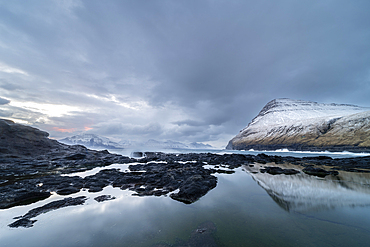 Snow covered mountains and rock pool reflections at low tide, Gjogv village, Eysturoy Island, Faroe Islands, Denmark, Europe