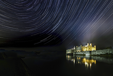 Leeds castle illuminated reflected in moat showing star trails in the night sky, near Maidstone, Kent, England, United Kingdom, Europe