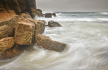 Atlantic surf rolls across granite shoreline rocks, at Porthgwarra Cove, near Land's End, in the far west of Cornwall, Great Britain.