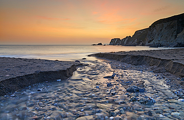 A stream cuts across sand as it reaches the sea, at dusk, in Ayrmer Cove, a remote cove near Kingsbridge, south coast of Devon, England, United Kingdom, Europe