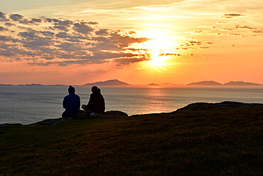 Two tourists enjoying a beautiful sunset at Neist Point on the Isle of Skye, Inner Hebrides, Scotland, United Kingdom, Europe