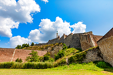 Ground-level wide-angle view of Kalemegdan Fortress stone walls rising above grassy slopes under bright blue skies. Horizontal landscape orientation.