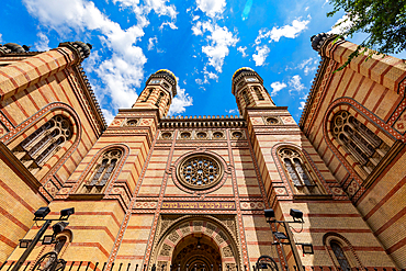 Facade and twin towers of the Dohány Street Synagogue, the largest synagogue in Europe. Low-angle view looking up at the Dohány Street Synagogue facade and towers under a blue sky. Captured in vertical portrait orientation.