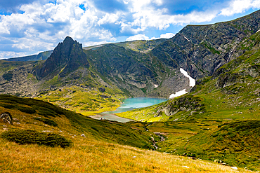 Horizontal, eye-level shot of The Tear Lake in the Seven Rila Lakes area, near Sapareva Banya, Bulgaria. Lake surrounded by steep rocky peaks and grassy slopes.