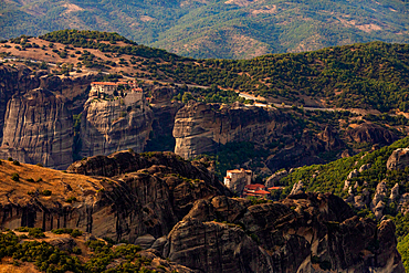 Aerial view in landscape orientation of Meteora’s monasteries perched atop towering rock pillars, surrounded by rugged cliffs and green hills, Thessaly, Greece.