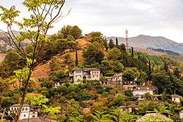 Landscape orientation view of hillside homes and greenery with mountains in the background in Gjirokastër, Gjirokastër County, Albania.