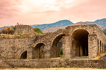 Landscape orientation view of the stone archways of Gjirokastër Castle at sunset, with mountains in the background and warm tones in the sky, Gjirokastër, Albania.