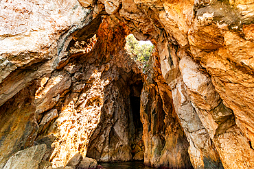 Inside view of a rock arch and sea cave along the Ionian Sea near Dhermi, Vlorë County, Albania, with sunlight illuminating the textured stone walls.