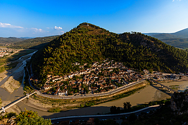 Panoramic aerial view of the Gorica neighborhood wrapped around the bend of the Osum River in Berat, Berat County, Albania, with tree-covered hills and connecting bridges seen from Kala Castle.