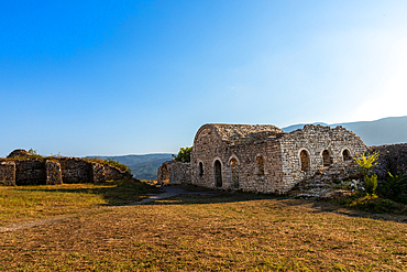 Stone remains of a Byzantine church within the fortified grounds of Kala Castle in Berat, Berat County, Albania, surrounded by mountain views and open grassy terrain.