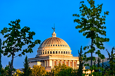 The domed roof of the Resurrection of Christ Orthodox Cathedral in Berat, Berat County, Albania, framed by trees and glowing in the warm light of sunset.