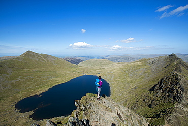 A woman stands on top of Striding Edge with a view of Red Tarn below and Ullswater in the far distance, Lake District National Park, Cumbria, England, United Kingdom, Europe