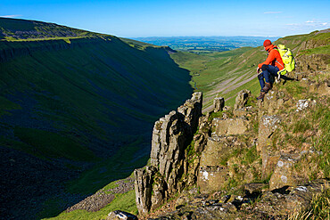 A man hiking the Pennine Way sits on the edge of the huge escarpment called Highcup Nick in the Yorkshire Dales, Yorkshire, England, United Kingdom, Europe