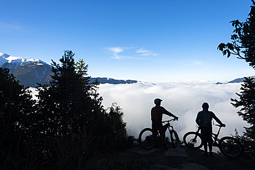 Mountain bikers look out across a valley filled with a cloud inversion in the Himalayas while biking in the Gosainkund region, Langtang region, Nepal, Asia