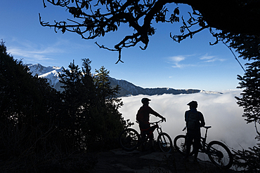 Mountain bikers look out across a valley filled with a cloud inversion in the Himalayas while biking in the Gosainkund region, Langtang region, Nepal, Asia