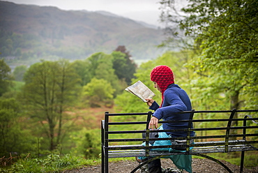 A woman rests on a bench while walking in The Lake District near Grasmere, Cumbria, England, United Kingdom, Europe