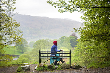 A woman rests on a bench while walking in The Lake District near Grasmere, Cumbria, England, United Kingdom, Europe