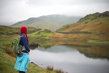 A woman looks out over Alcock Tarn near Grasmere, Lake District, Cumbria, England, United Kingdom, Europe