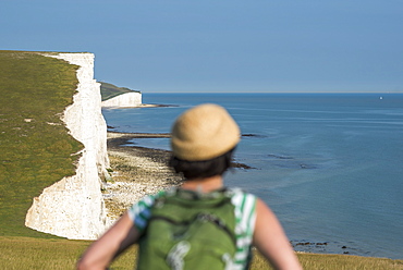 A woman looks out over the cliffs with views of the Seven Sisters coastline in the distance, South Downs National Park, East Sussex, England, United Kingdom, Europe