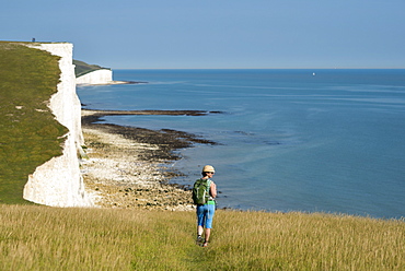 A woman walks along the cliffs near Beachy Head with views of the Seven Sisters coastline in the distance, South Downs National Park, East Sussex, England, United Kingdom, Europe