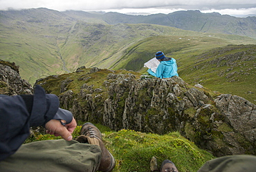 A woman checks her map while looking towards Great Langdale valley from the Langdale Pikes, Lake District National Park, Cumbria, England, United Kingdom, Europe