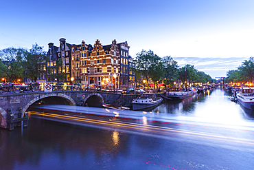 Dusk on Brouwersgracht Canal with trailing light from a tourist boat passing under a bridge, Amsterdam, North Holland, The Netherlands, Europe