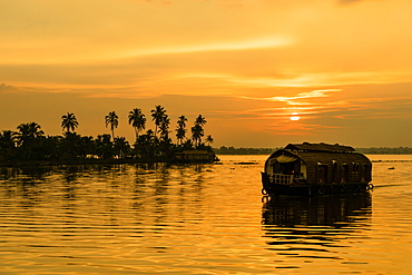 A traditional houseboat moves past the setting sun on the Kerala Backwaters, Kerala, India, Asia