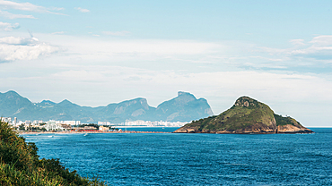 Picturesque Ocean view with Lush Green Island and Cityscape against Mountains on a sunny day, looking towards Pedra do Pombal and Barra da Tijuca, Rio de Janeiro, Brazil, South America