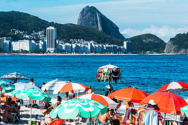 Man selling swimsuits at Copacabana Beach with iconic Sugarloaf mountain in far background, Rio de Janeiro, Brazil, South America