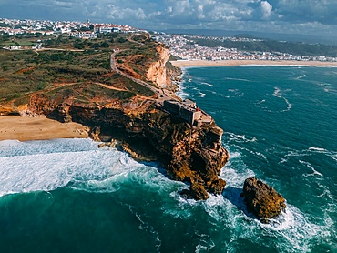 Tourists gather at the historic São Miguel Arcanjo lighthouse overlooking Nazaré's stunning coastline with giant waves, enjoying spectacular views of the ocean waves on a sunny day