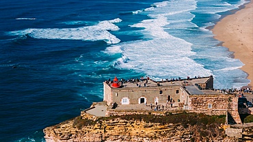 Aerial view of tourists at the historic Sao Miguel Arcanjo lighthouse overlooking Nazare's stunning coastline with giant waves, enjoying spectacular views, Nazare, Oeste, Estremadura, Portugal, Europe