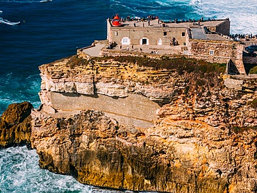 Aerial view of tourists at the historic Sao Miguel Arcanjo lighthouse overlooking Nazare's stunning coastline with giant waves, enjoying spectacular views, Nazare, Oeste, Estremadura, Portugal, Europe