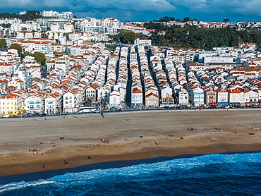 The lively beach of Nazaré, Portugal, revealing rows of charming houses with red roofs and people enjoying the sandy shore under a clear sky