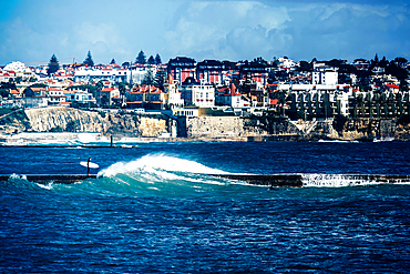 Surfer on a pier with stormy seas with Cascais Estoril buildings in the background just outside of Lisbon, Portugal, Europe