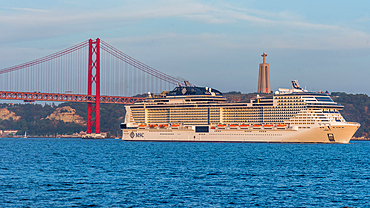 Large cruise ship belonging to the MSC Group passes the 25 April Bridge in Lisbon, Portugal on the Tagus with Rei Cristo statue in the background