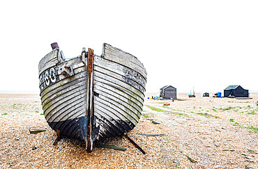 An old fishing boat lies on the beach.with fishermans huts in the background, Dungeness, Kent, England, United Kingdom, Europe