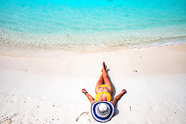 woman with straw hat sunbathing on tropical beach