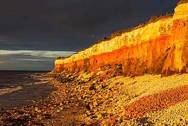 Dramatic golden hour seascape of Hunstanton cliffs with dark stormy sky, on North Norfolk coast, Norfolk, East Anglia, England, United Kingdom, Europe