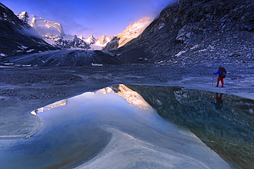 Hiker looks at sunrise from a pond at Forno Glacier, Forno Valley, Maloja Pass, Engadine, Graubunden, Switzerland, Europe