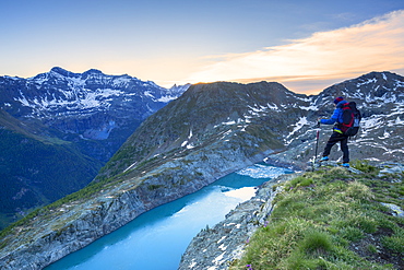 A hiker looks at Lake Pirola from above at sunrise, Chiareggio valley, Valmalenco, Valtellina, Lombardy, Italy, Europe