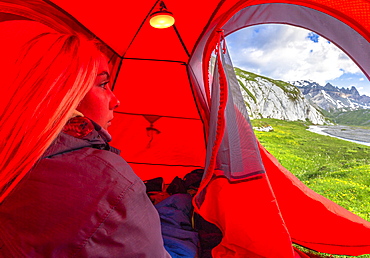 Young girls looks out of a red tent, Unterer Segnesboden, Flims, District of Imboden, Canton of Grisons (Graubunden), Switzerland, Europe