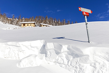 Traditional huts with trekking signal in winter, Livigno, Valtellina, Lombardy, Italy, Europe