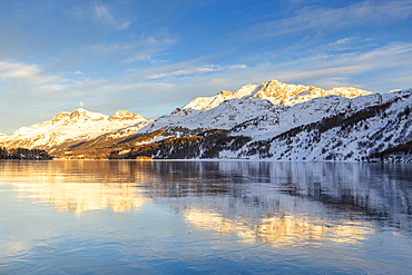 Mountains illuminated by sun at sunset reflected on the icy surfaces of Lake Sils, Engadine, Graubunden, Switzerland, Europe