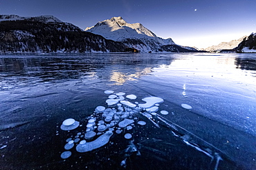 Methane bubbles in the icy surface of the lake with snowy peak illuminated by moonlight, Sils, Engadine Valley, Graubunden, Swiss Alps, Switzerland, Europe